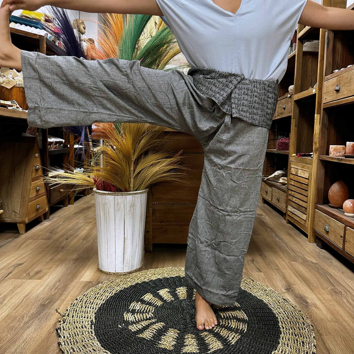 Person standing on one leg wearing unisex Thai Fisherman yoga pants, mandala mantra on grey