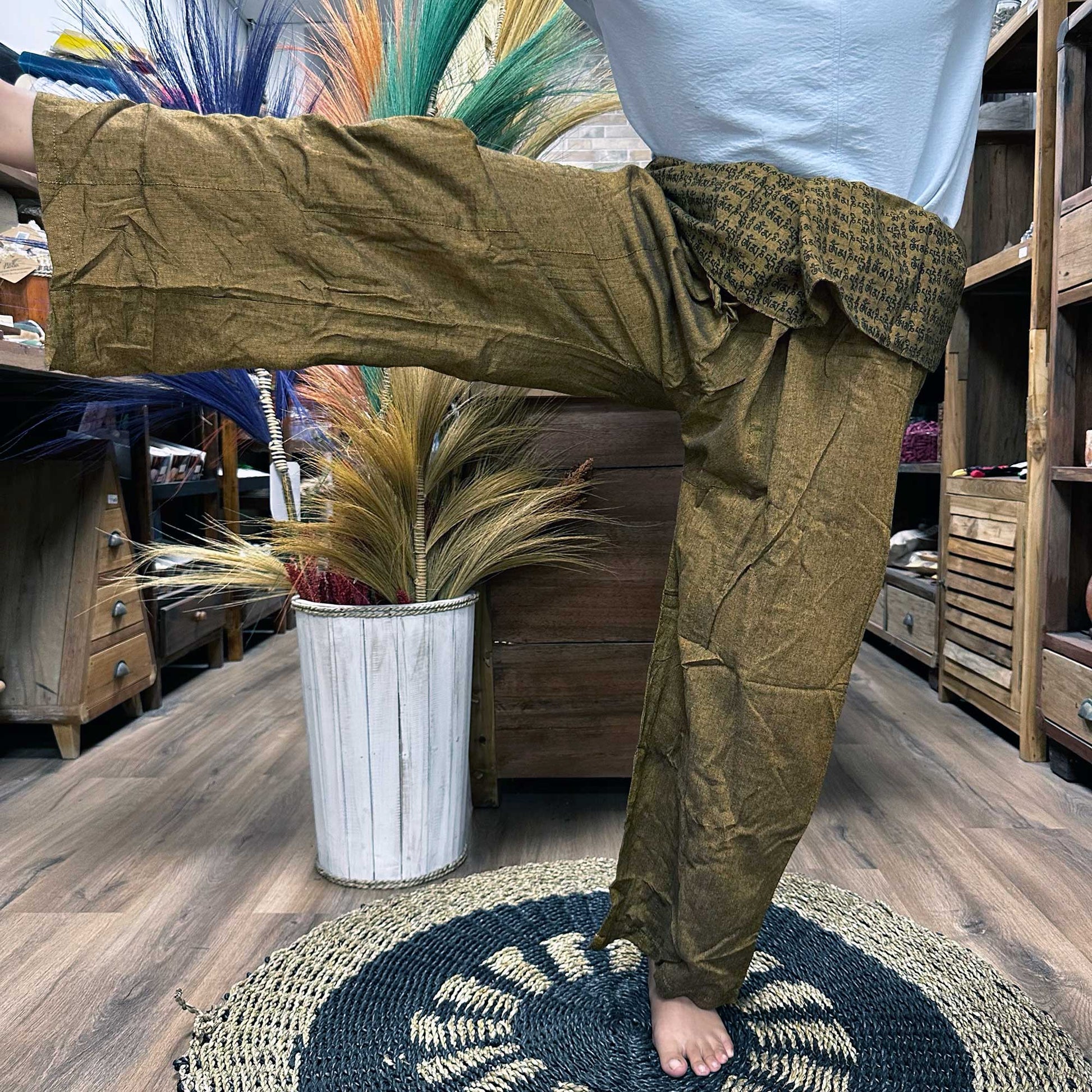 Person standing on one leg wearing unisex Thai Fisherman yoga pants made from 100% cotton, mandala mantra on orange