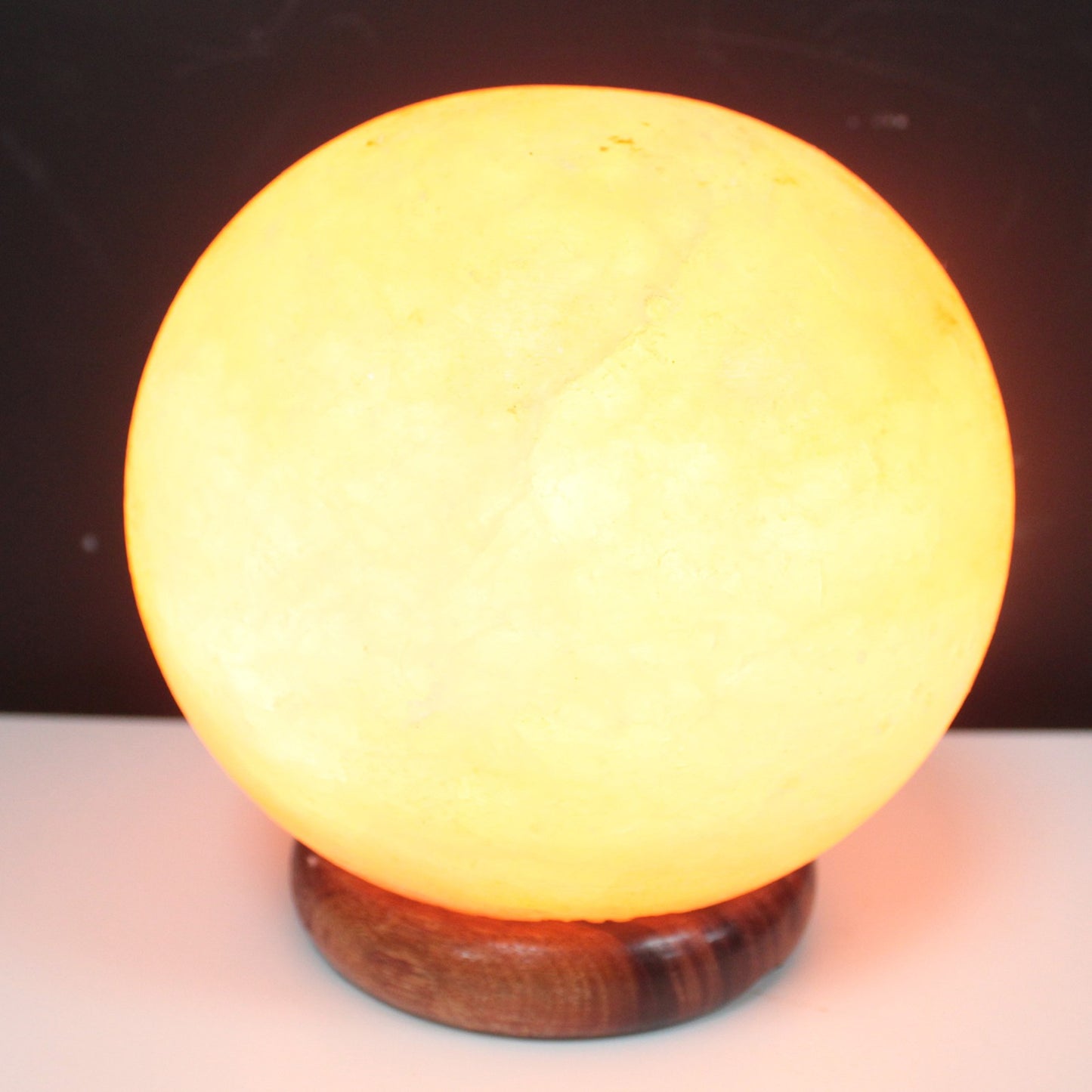 Image of brightly lit himalayan salt lamp ball with wooden base