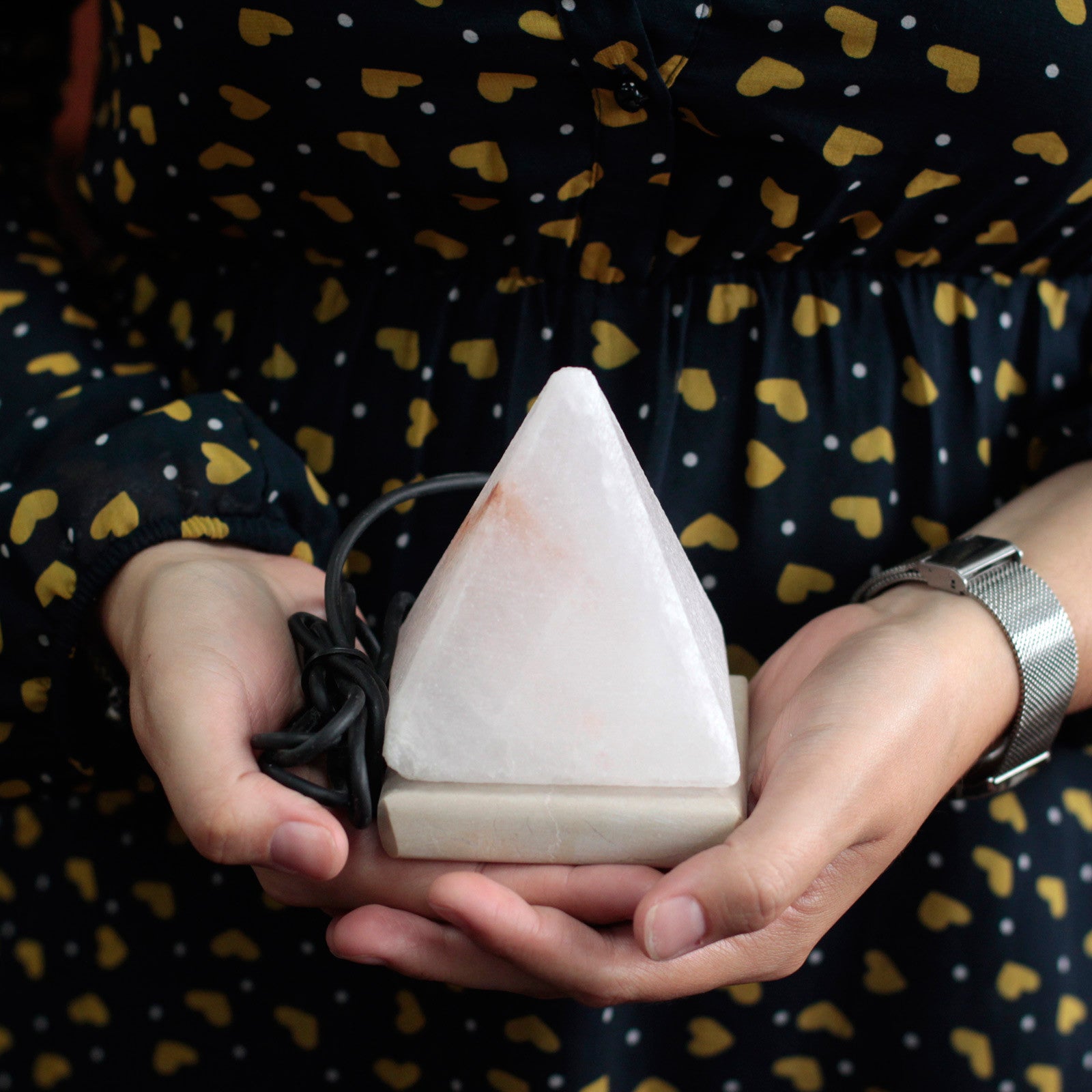 Image of pyramid salt lamp in palm of womens hands, showing stone base and usb connectors