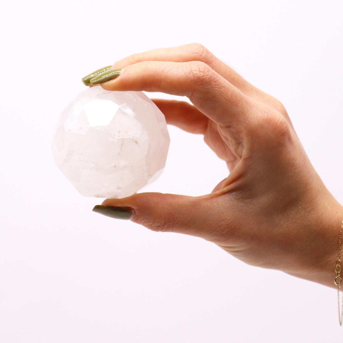 Image of gemstone faceted healing ball, rock quartz held in a hand for size, white background.