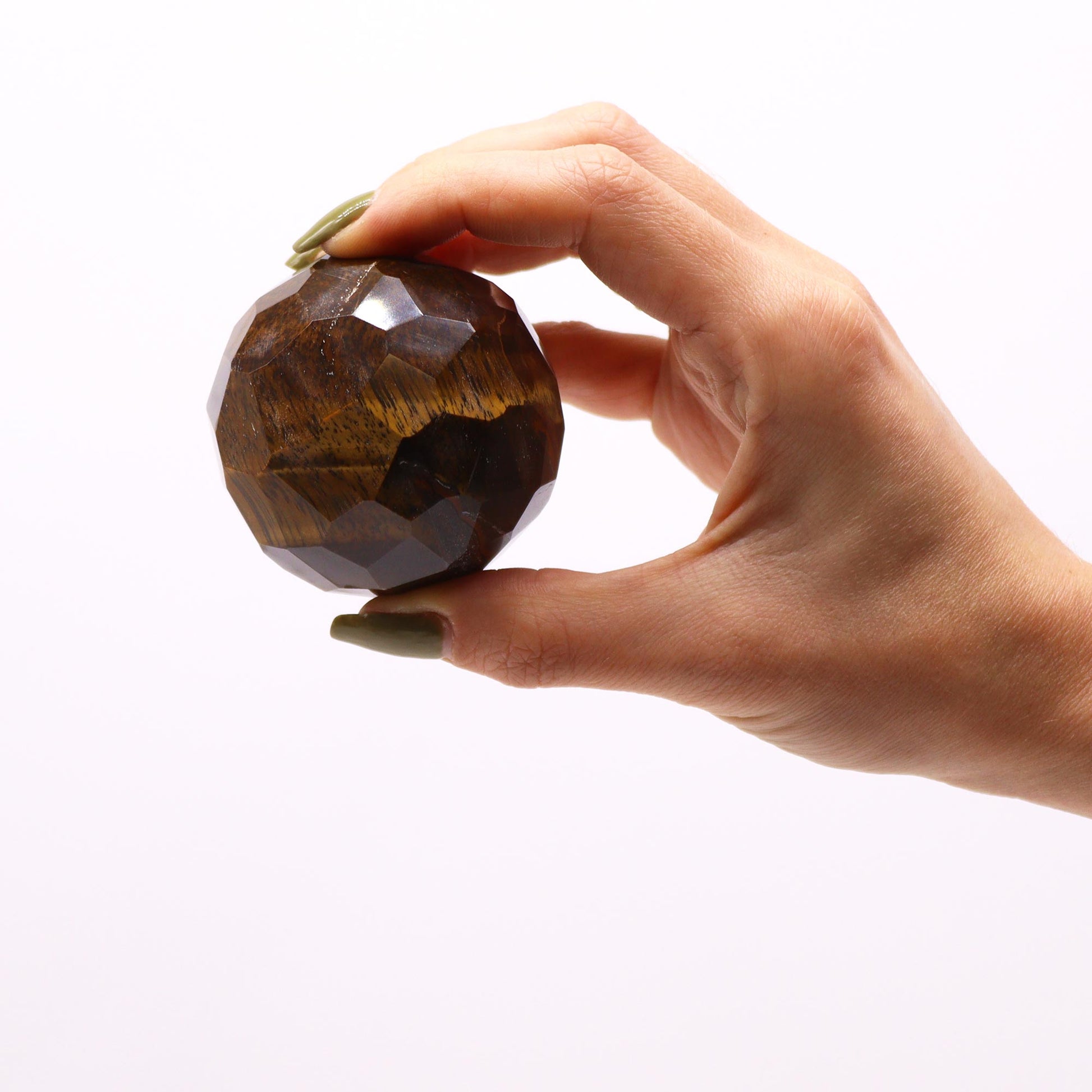 Image of gemstone faceted healing ball - tigereye stone in someones fingers against a white background showing size against human hand